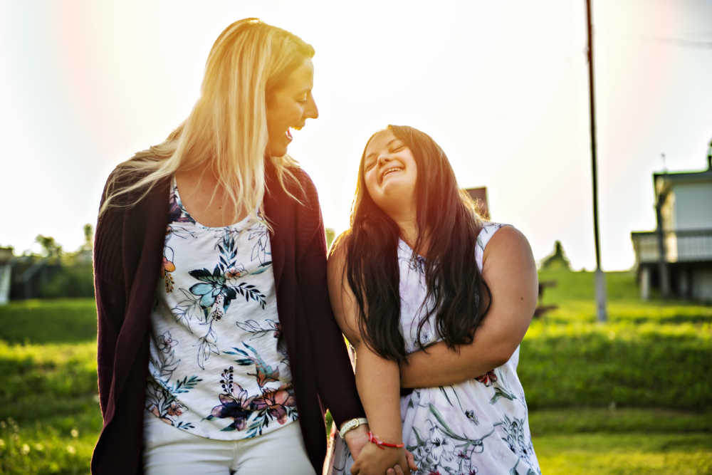 A Portrait of trisomie 21 adult girl smilin outside at sunset with family friend